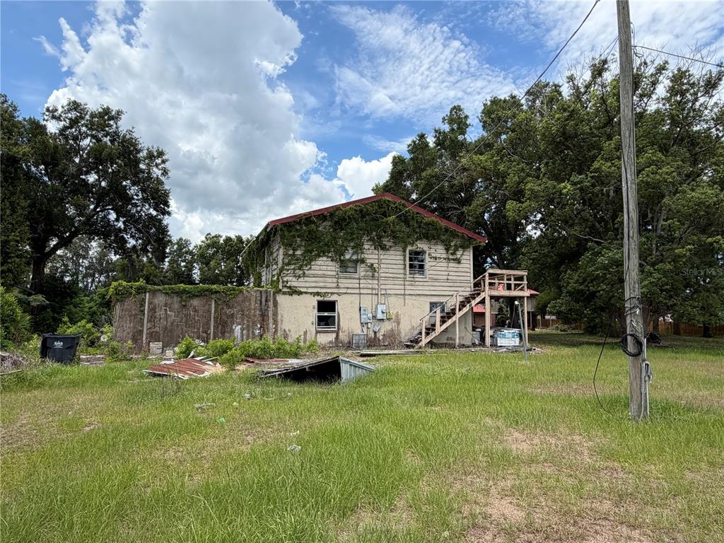 A two-story house with exterior stairs and overgrown vines stands in a grassy lot — 4215 STEARNS ROAD, VALRICO, FL