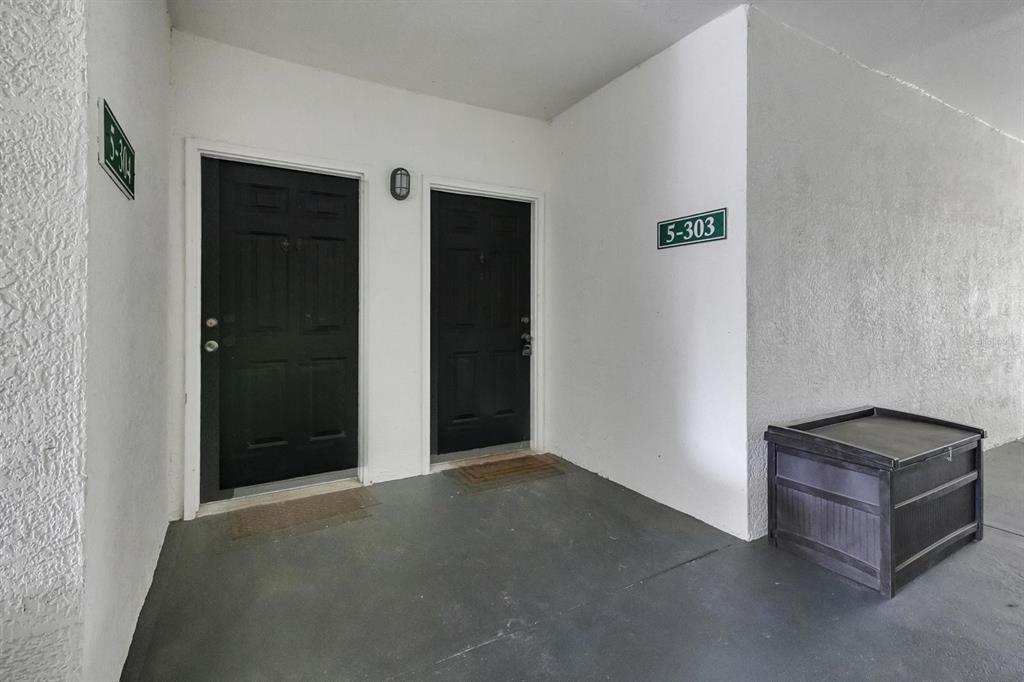 Two black doors are situated on a covered walkway next to a storage chest — 2705 MAITLAND CROSSING WAY UNIT 303, ORLANDO, FL