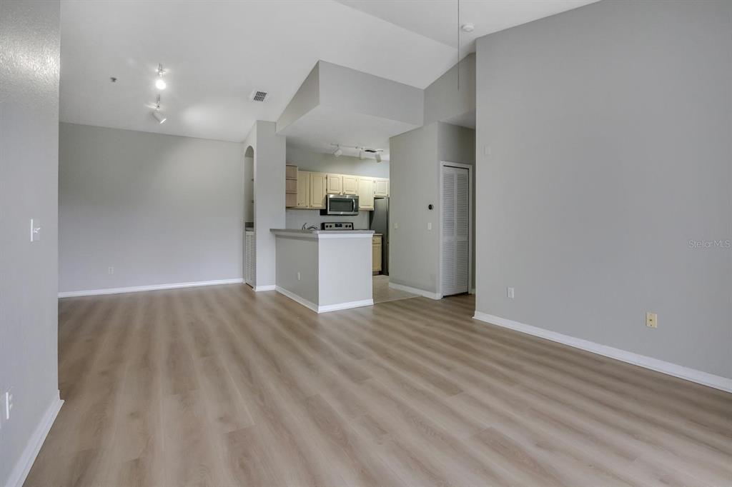 An open-concept living area features light wood-look flooring, gray walls, and a kitchen with cabinets — 2705 MAITLAND CROSSING WAY UNIT 303, ORLANDO, FL