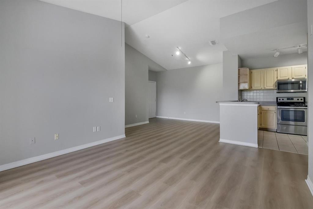 An open-concept living area with light wood-look flooring leads into a kitchen with stainless appliances — 2705 MAITLAND CROSSING WAY UNIT 303, ORLANDO, FL
