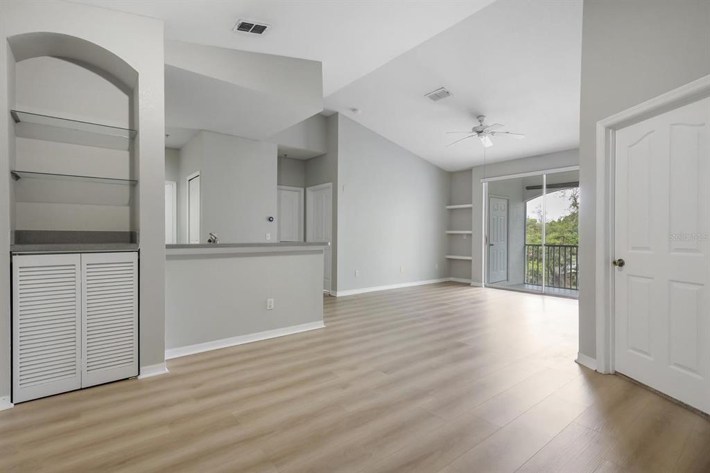 An open-concept living room features light wood-look flooring, vaulted ceilings, built-in shelving, and a balcony — 2705 MAITLAND CROSSING WAY UNIT 303, ORLANDO, FL