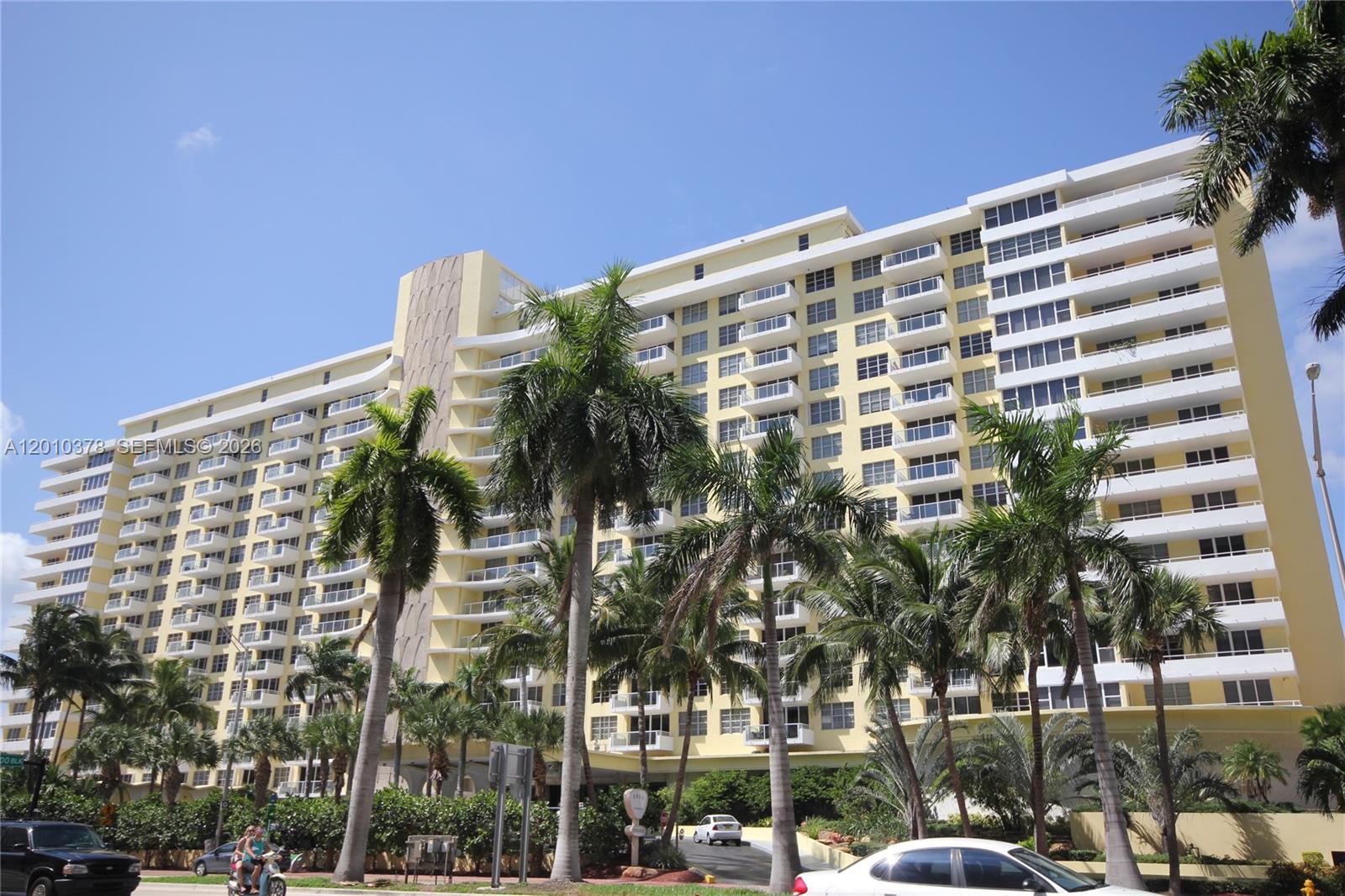 A multi-story yellow residential building stands behind a row of palm trees — 5600 Collins Ave # 9E, Miami Beach FL 33140, MIAMI BEACH, FL