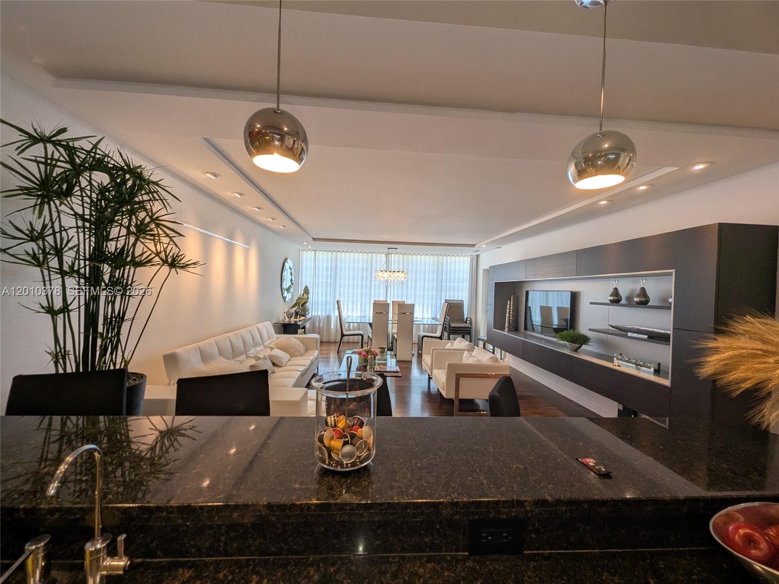 A modern living and dining room features a dark granite kitchen island in the foreground — 5600 Collins Ave # 9E, Miami Beach FL 33140, MIAMI BEACH, FL