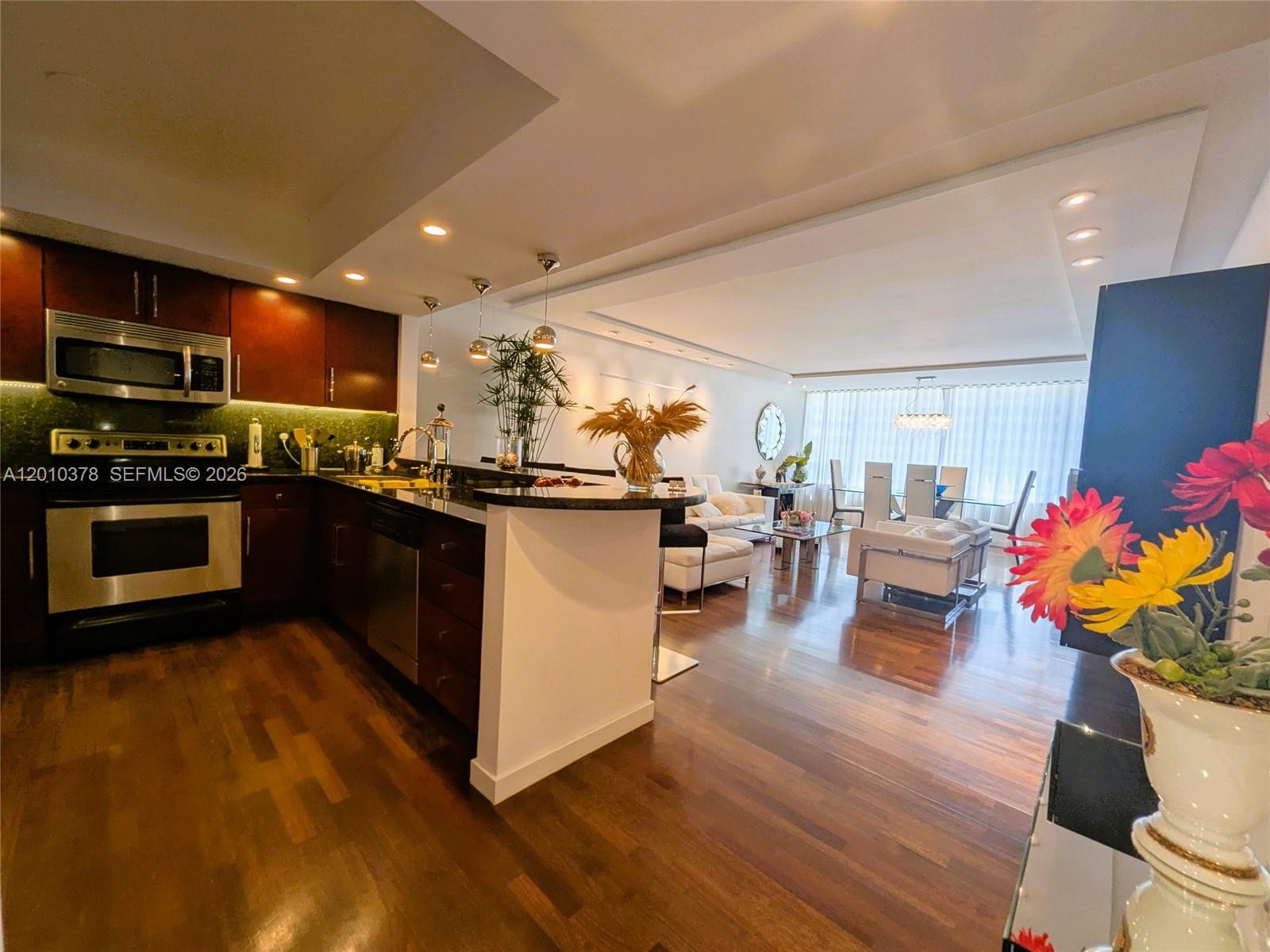 A modern kitchen with dark wood cabinets and a breakfast bar opens into a living area — 5600 Collins Ave # 9E, Miami Beach FL 33140, MIAMI BEACH, FL