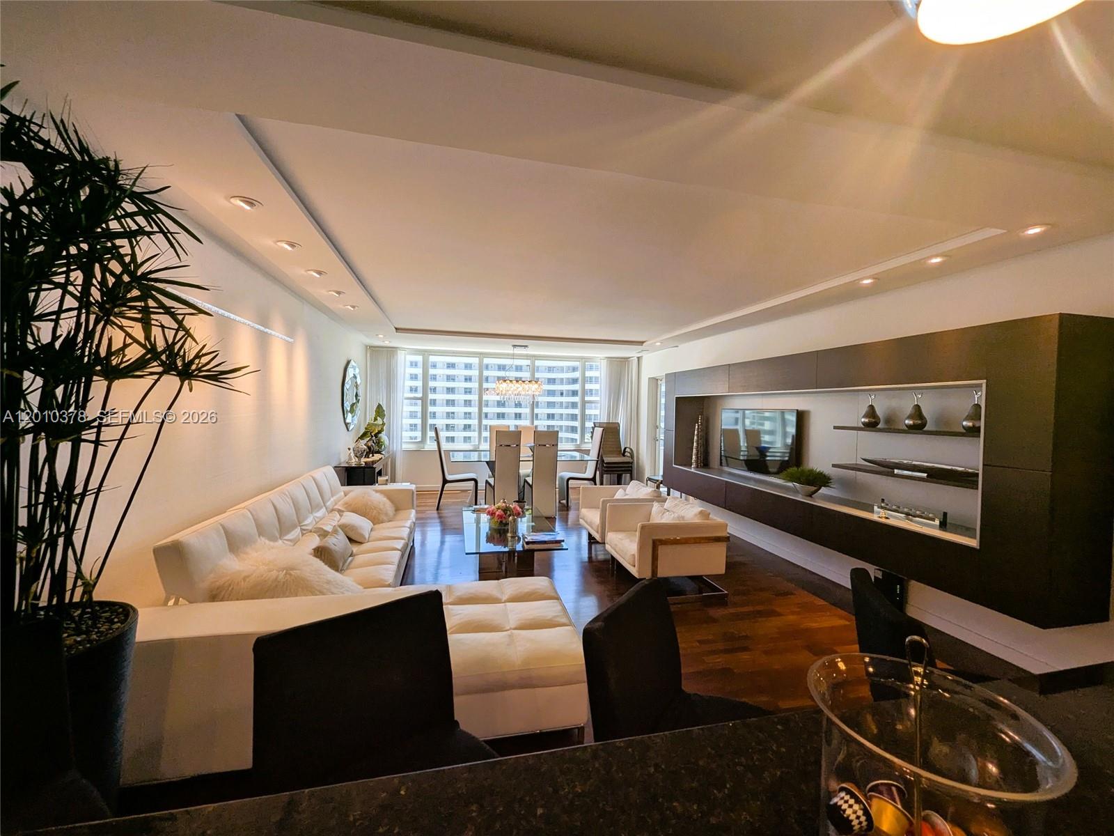 A modern living room features a white sectional sofa, dark wood floors, and a media wall — 5600 Collins Ave # 9E, Miami Beach FL 33140, MIAMI BEACH, FL