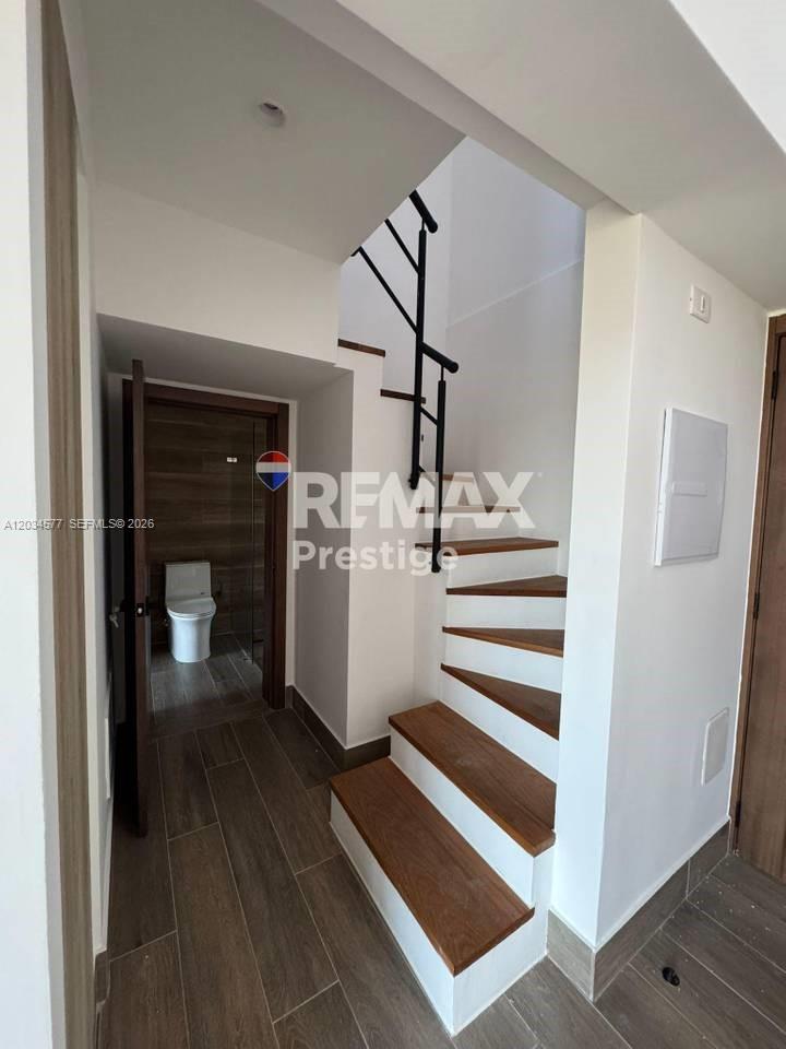 A staircase with wooden treads and a black metal railing leads upward beside a bathroom — 1 La altagracia # 1, FL