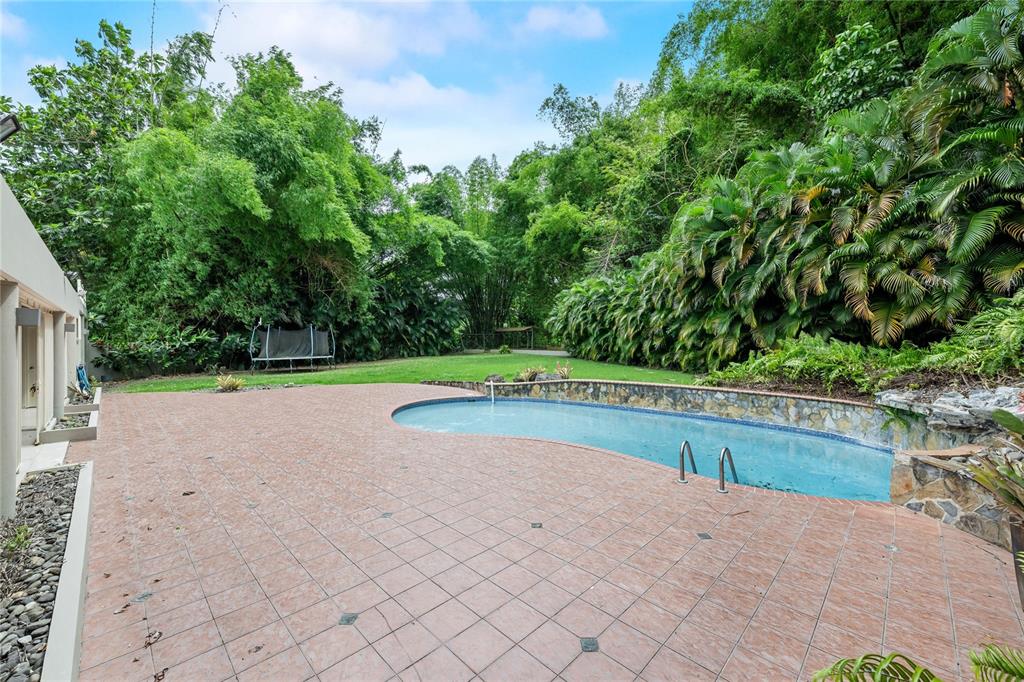 A backyard features a tiled patio, a curved swimming pool, and a lush, tree-lined lawn — Street #1 STREET #1 TINTILLO HILLS URB. UNIT 606, GUAYNABO, PR
