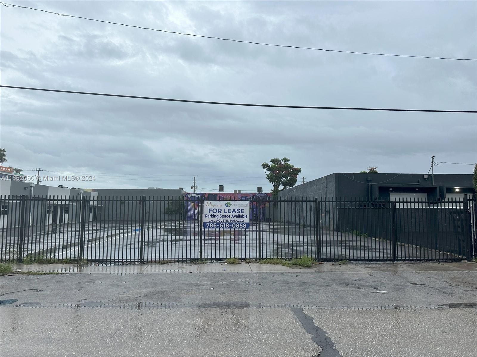 A fenced-in paved parking lot is situated between two industrial buildings under a cloudy sky — 1740 NW 22nd St, Miami FL 33142, MIAMI, FL