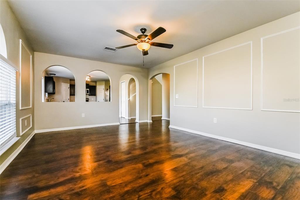 A living room with dark wood floors, arched wall openings, and decorative wall molding — 10405 FLY FISHING STREET, RIVERVIEW, FL