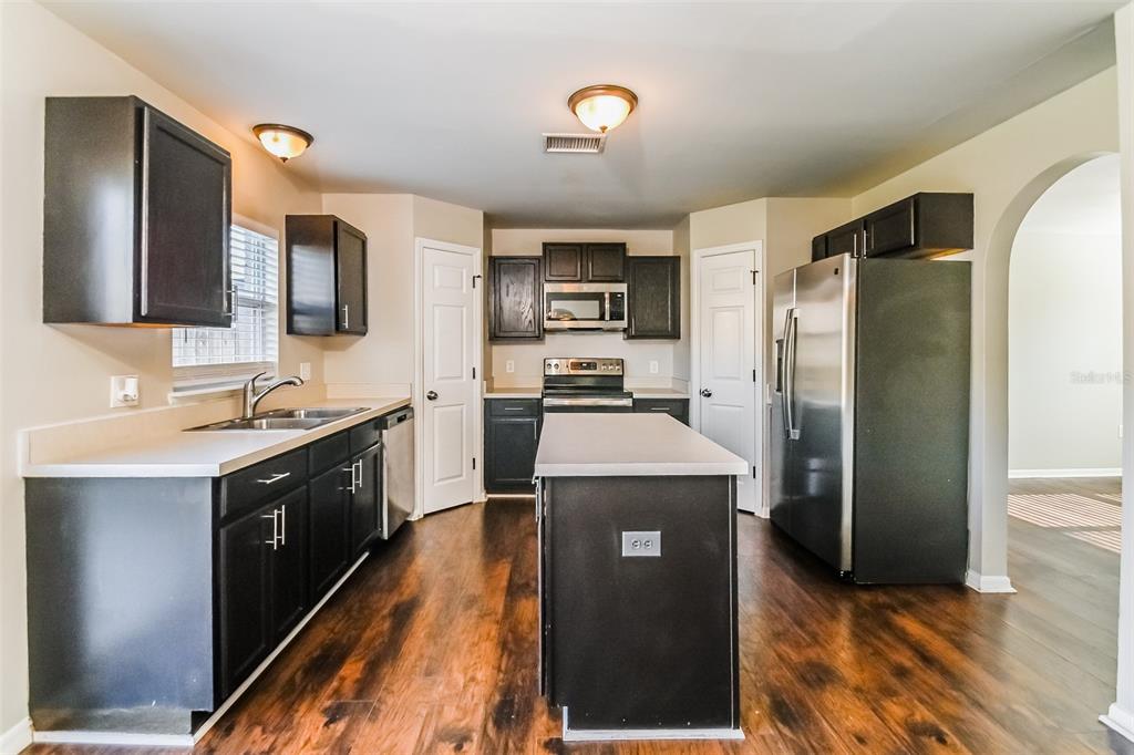 A kitchen features dark cabinets, stainless steel appliances, a center island, and wood-look flooring — 10405 FLY FISHING STREET, RIVERVIEW, FL
