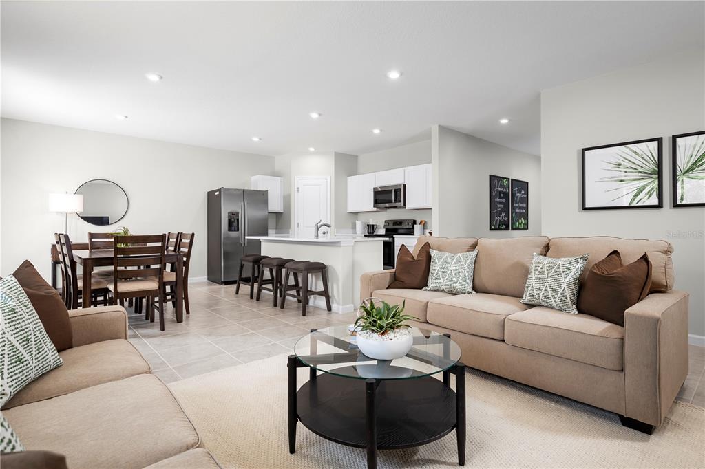An open-concept living room and kitchen featuring neutral furniture, tile flooring, and white cabinetry — 6951 SUNDIAL DRIVE, LAKELAND, FL