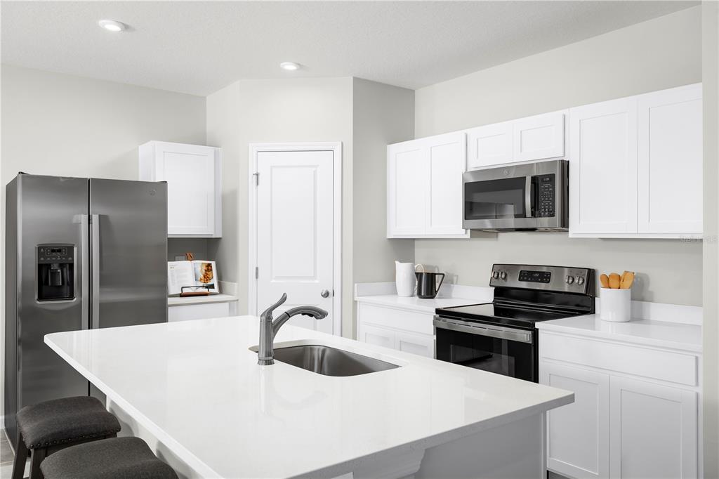 A modern kitchen features white cabinets, stainless steel appliances, and a large central island — 6951 SUNDIAL DRIVE, LAKELAND, FL