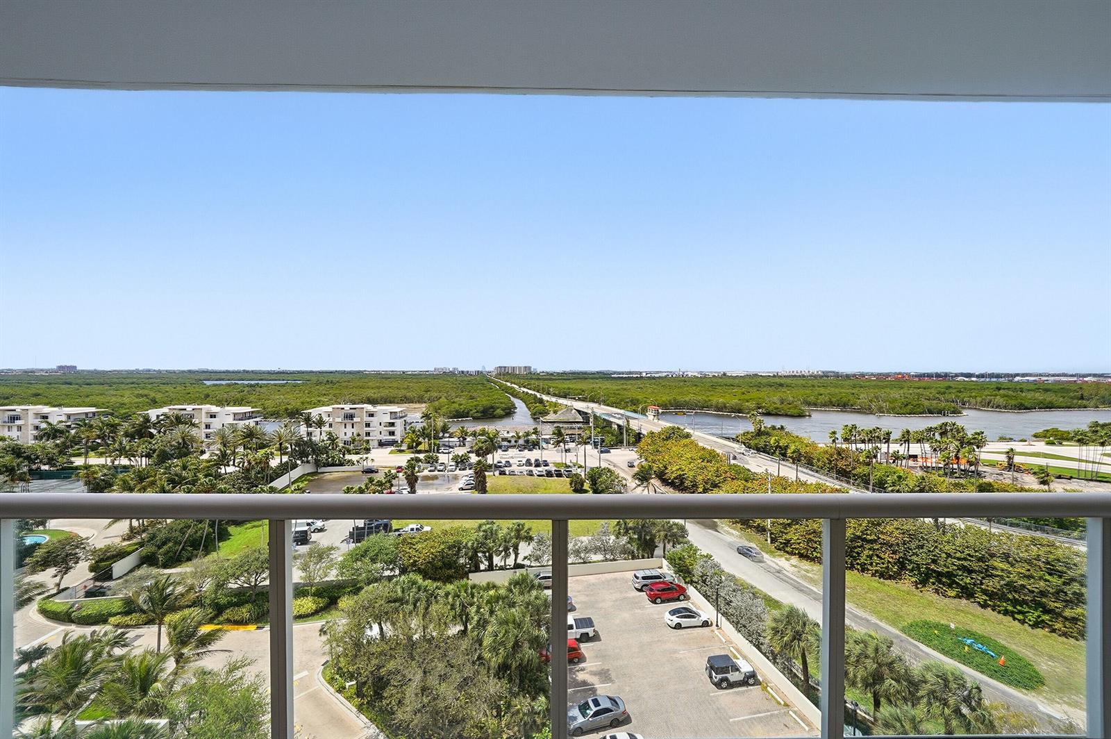 An elevated balcony view overlooks a parking lot, lush greenery, a bridge, and distant water — 6051 N Ocean Drive # 1003, Hollywood FL 33019, HOLLYWOOD, FL