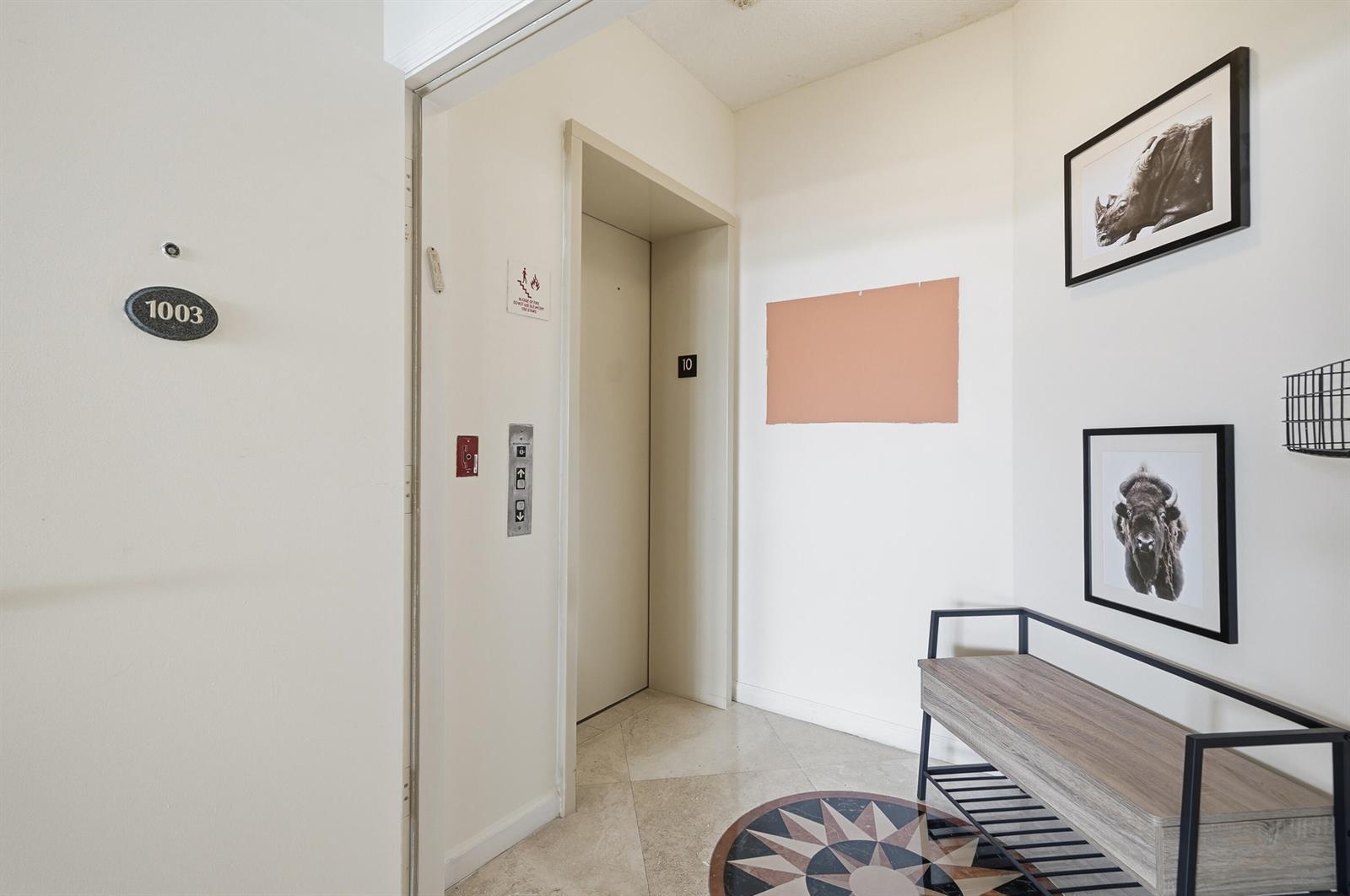 An elevator lobby with a numbered door, tiled floor, and wall-mounted artwork and furniture — 6051 N Ocean Drive # 1003, Hollywood FL 33019, HOLLYWOOD, FL