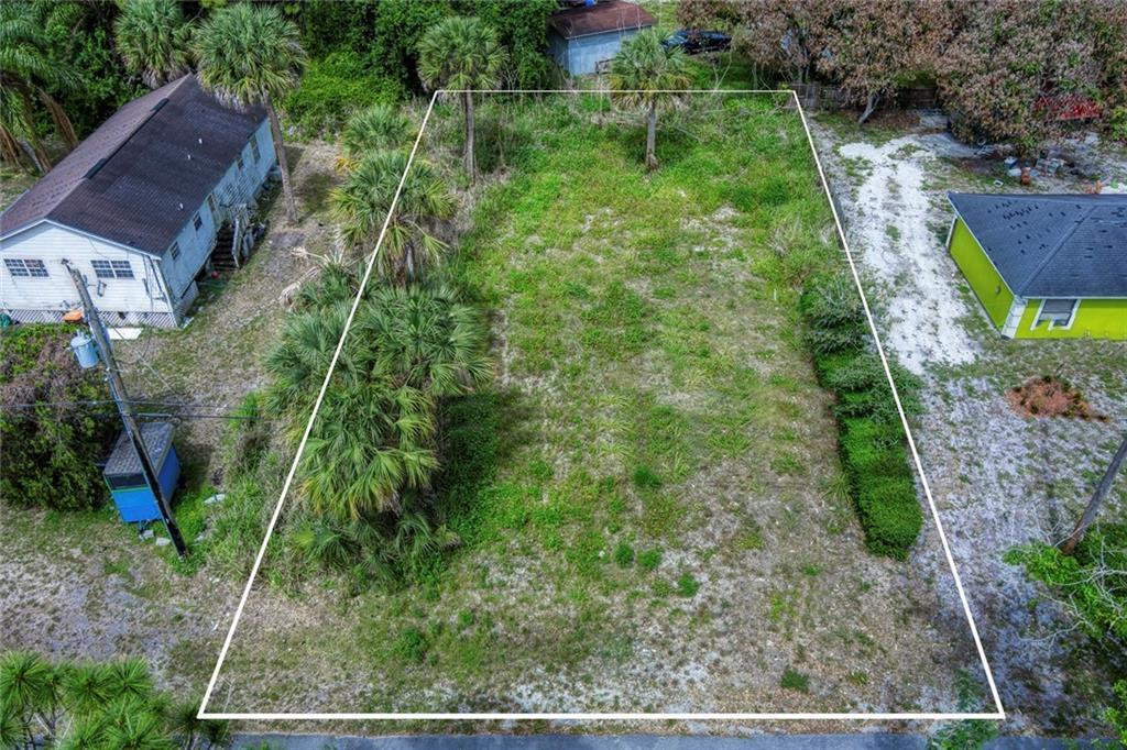 An aerial view shows a rectangular, grass-covered vacant lot bordered by trees and neighboring houses — VERO BEACH, FL