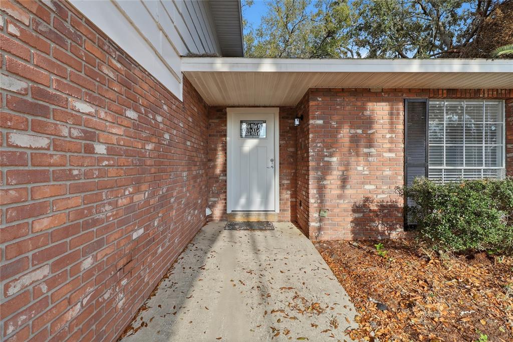 A concrete walkway leads to a white front door set in a red brick exterior — 148 LAKE OTIS ROAD, WINTER HAVEN, FL