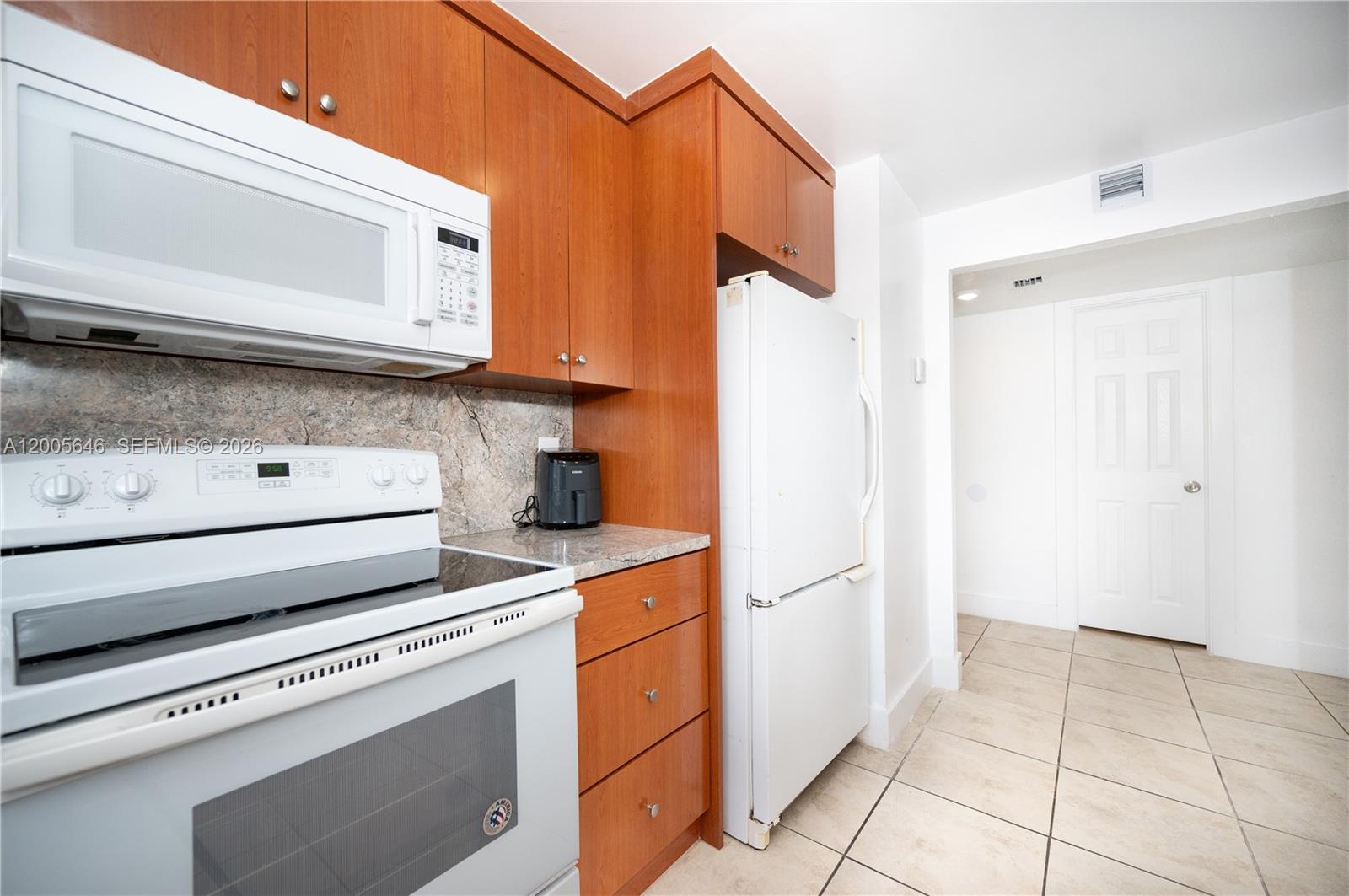 A kitchen features wood cabinets, white appliances, granite countertops, and light-colored tile flooring — 500 NE 26th St # 5D, Miami FL 33137, MIAMI, FL