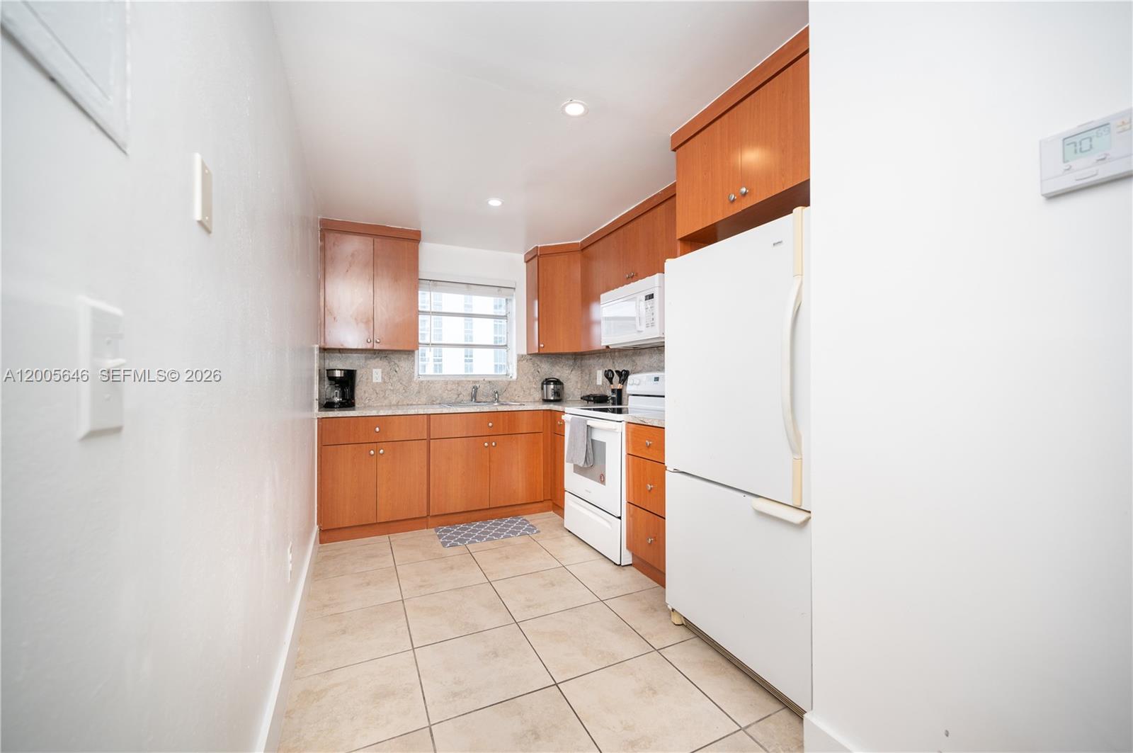 A galley kitchen features wood cabinets, white appliances, and light-colored tile flooring — 500 NE 26th St # 5D, Miami FL 33137, MIAMI, FL