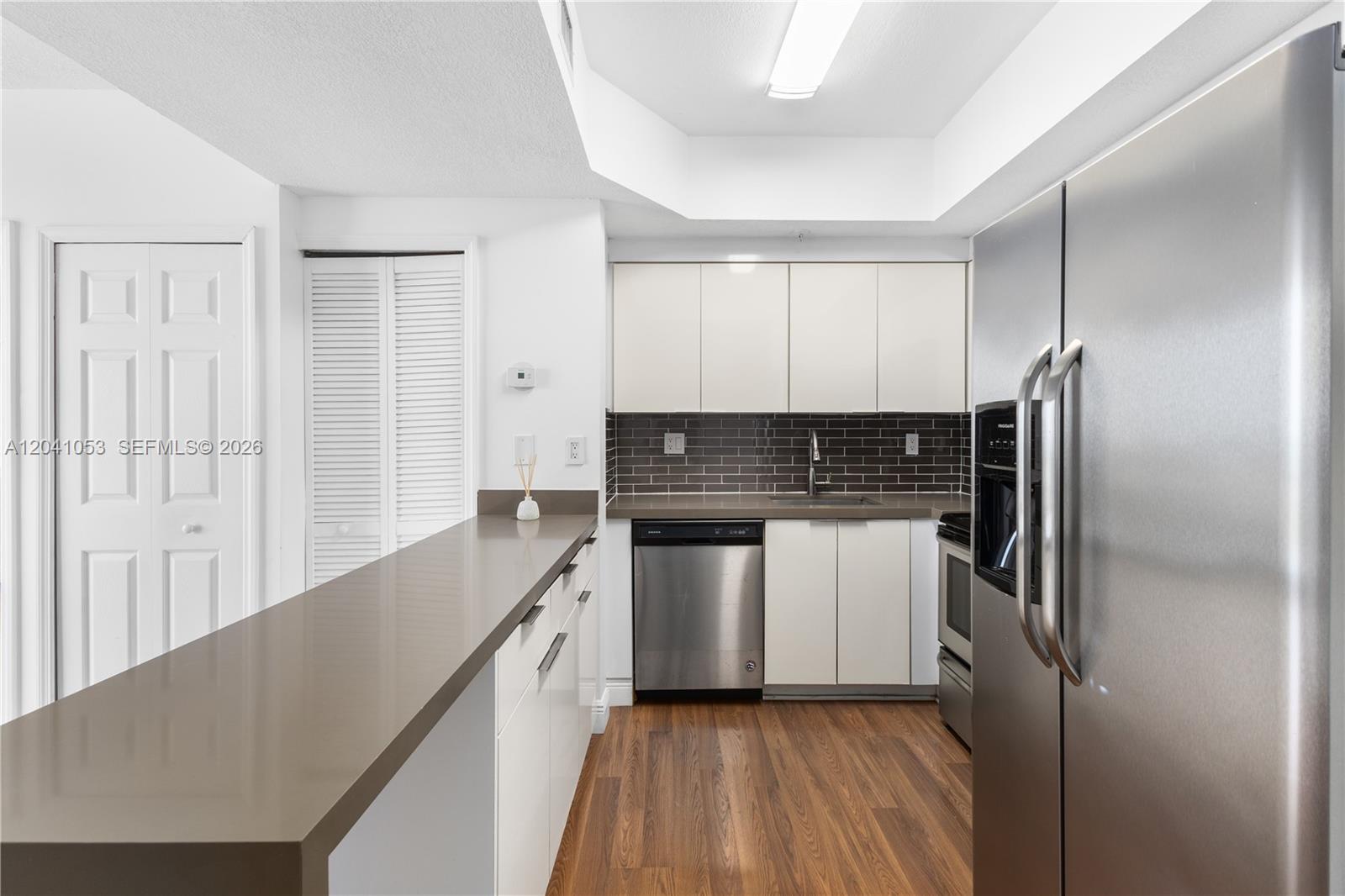 A kitchen features white cabinets, stainless steel appliances, a dark backsplash, and a breakfast bar — 3500 Coral Way # 1509, Miami FL 33145, MIAMI, FL