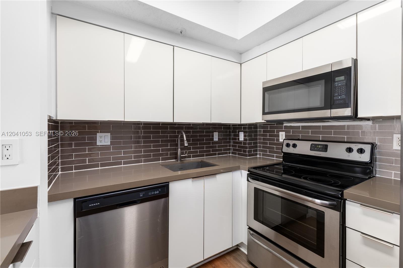 A modern kitchen features white cabinets, stainless steel appliances, and a dark tile backsplash — 3500 Coral Way # 1509, Miami FL 33145, MIAMI, FL