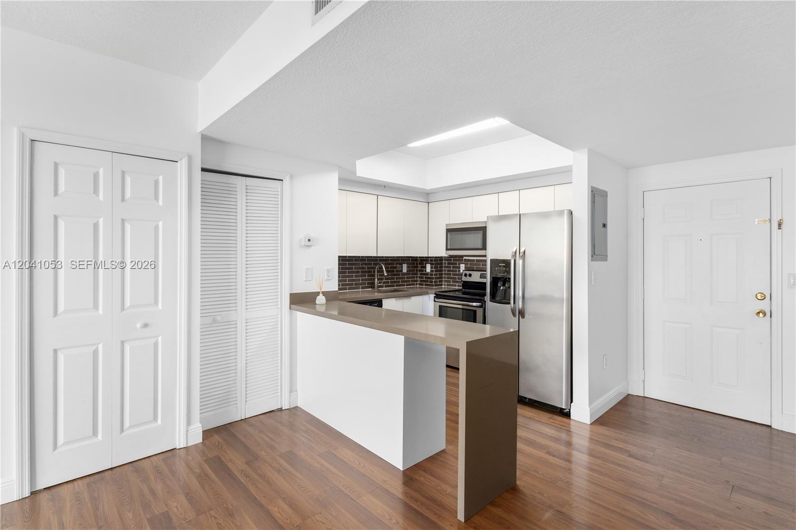 A kitchen features white cabinets, stainless steel appliances, a brown backsplash, and a breakfast bar — 3500 Coral Way # 1509, Miami FL 33145, MIAMI, FL