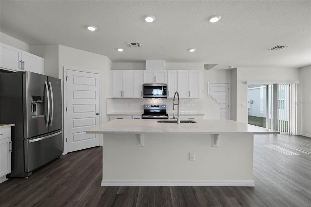 A modern kitchen features white cabinets, stainless steel appliances, and a large central island — 1734 HUMMINGBIRD ROAD, WINTER HAVEN, FL