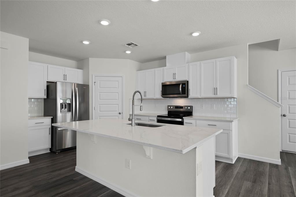 A modern kitchen features white cabinets, a marble-topped island, stainless steel appliances, and dark flooring — 1734 HUMMINGBIRD ROAD, WINTER HAVEN, FL