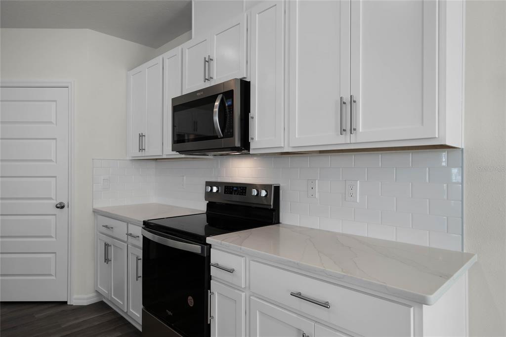 A kitchen features white cabinets, a black microwave and stove, and a white subway tile backsplash — 1734 HUMMINGBIRD ROAD, WINTER HAVEN, FL