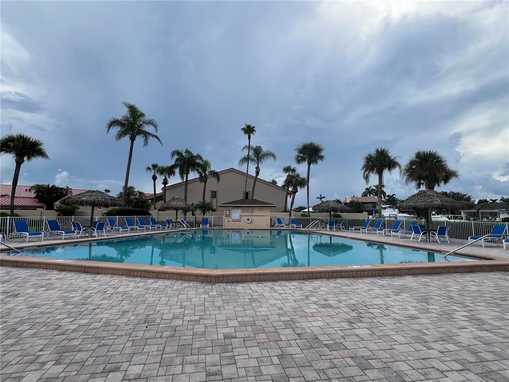 A swimming pool with lounge chairs and palm trees sits in front of a building — 4900 BRITTANY DRIVE S UNIT 305, ST PETERSBURG, FL