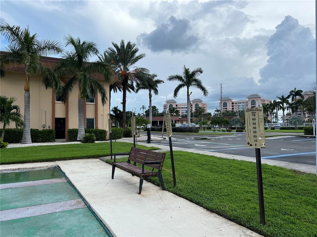 A wooden bench sits on a concrete walkway near a parking lot and palm trees — 4900 BRITTANY DRIVE S UNIT 305, ST PETERSBURG, FL