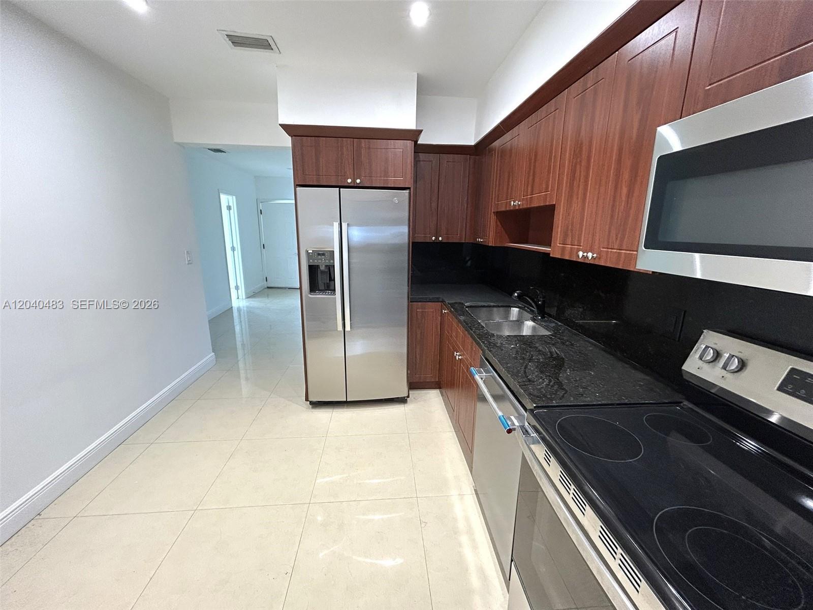 A kitchen features stainless steel appliances, dark wood cabinetry, and black granite countertops — 1530 NE 110th Ter # A3, Miami FL 33161, MIAMI, FL