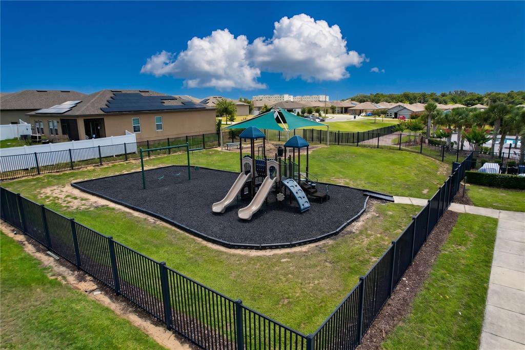 An outdoor playground with slides and swings is enclosed by a black metal fence — 148 LUDISIA LOOP, DAVENPORT, FL