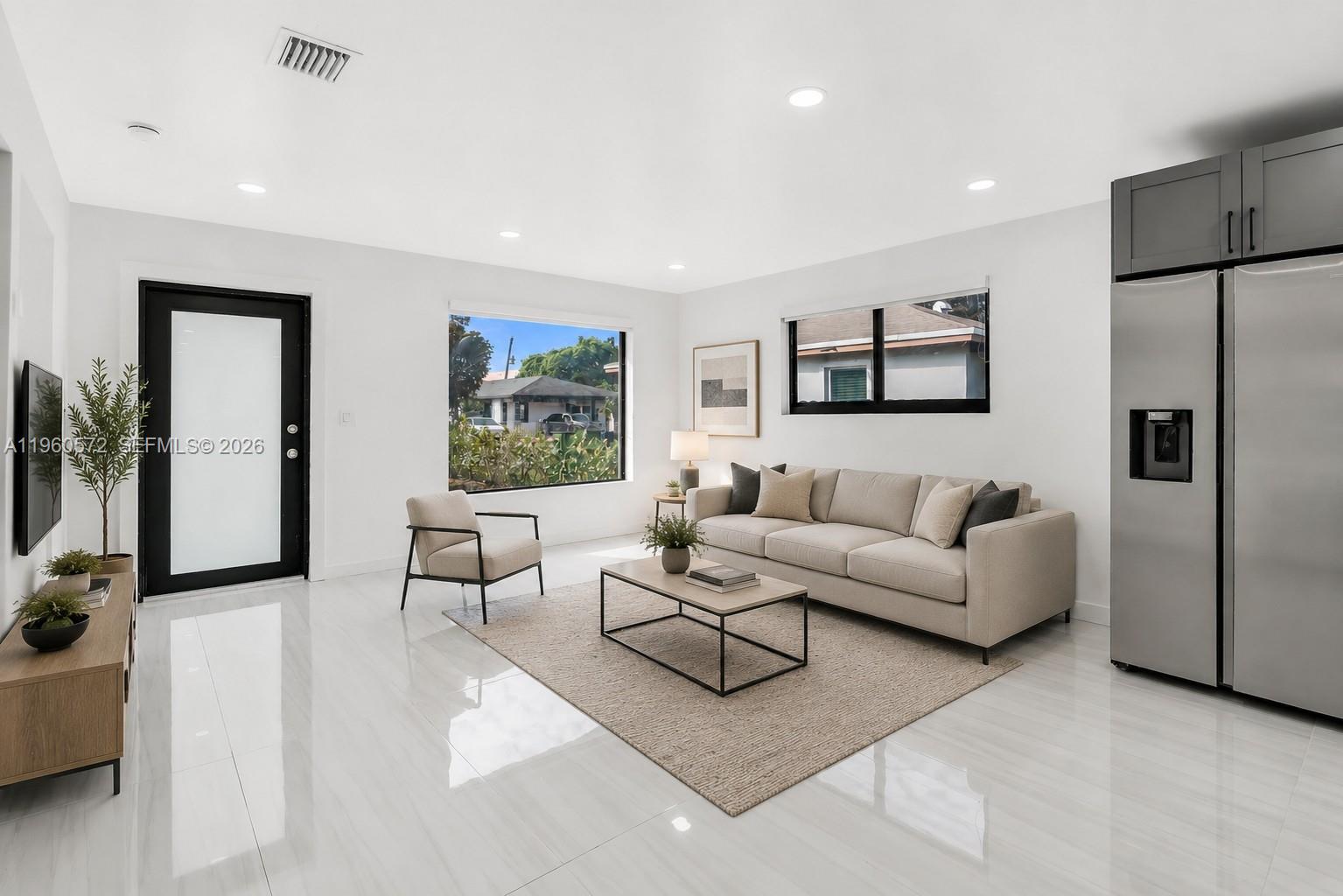 A modern living room features white tile floors, a beige sofa, and a large window — 528 NW 3rd Ct, Hallandale Beach FL 33009, HALLANDALE BEACH, FL
