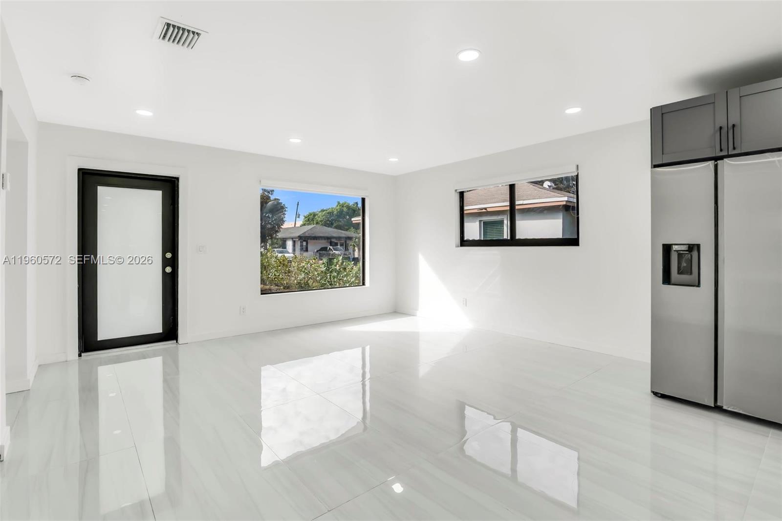 A bright, minimalist room features white tile flooring, a black-framed door, and a stainless refrigerator — 528 NW 3rd Ct, Hallandale Beach FL 33009, HALLANDALE BEACH, FL