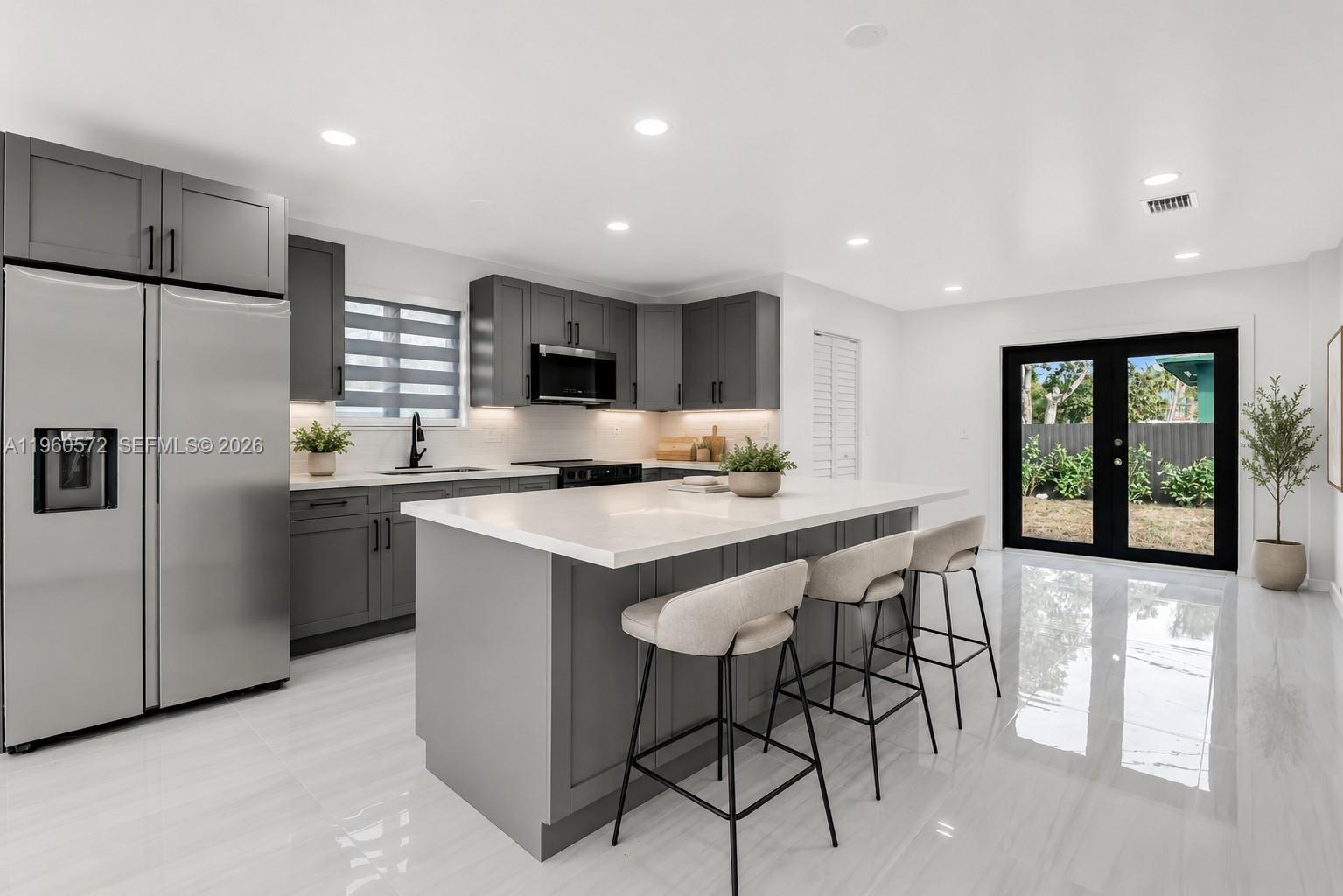 A modern kitchen features gray cabinets, a white quartz island, and stainless steel appliances — 528 NW 3rd Ct, Hallandale Beach FL 33009, HALLANDALE BEACH, FL