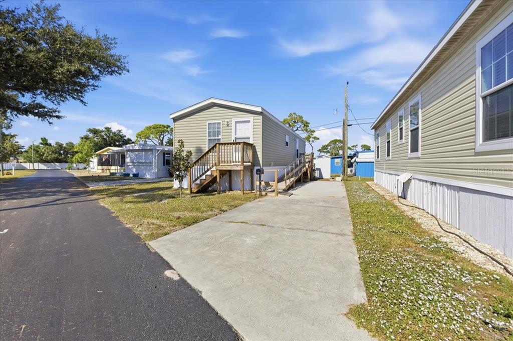 A light-colored manufactured home with a wooden porch and ramp sits beside a concrete driveway — 1800 ENGLEWOOD ROAD UNIT 166, ENGLEWOOD, FL