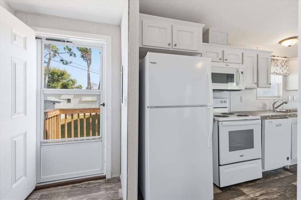 A kitchen with white appliances and cabinets next to a door leading to a deck — 1800 ENGLEWOOD ROAD UNIT 166, ENGLEWOOD, FL