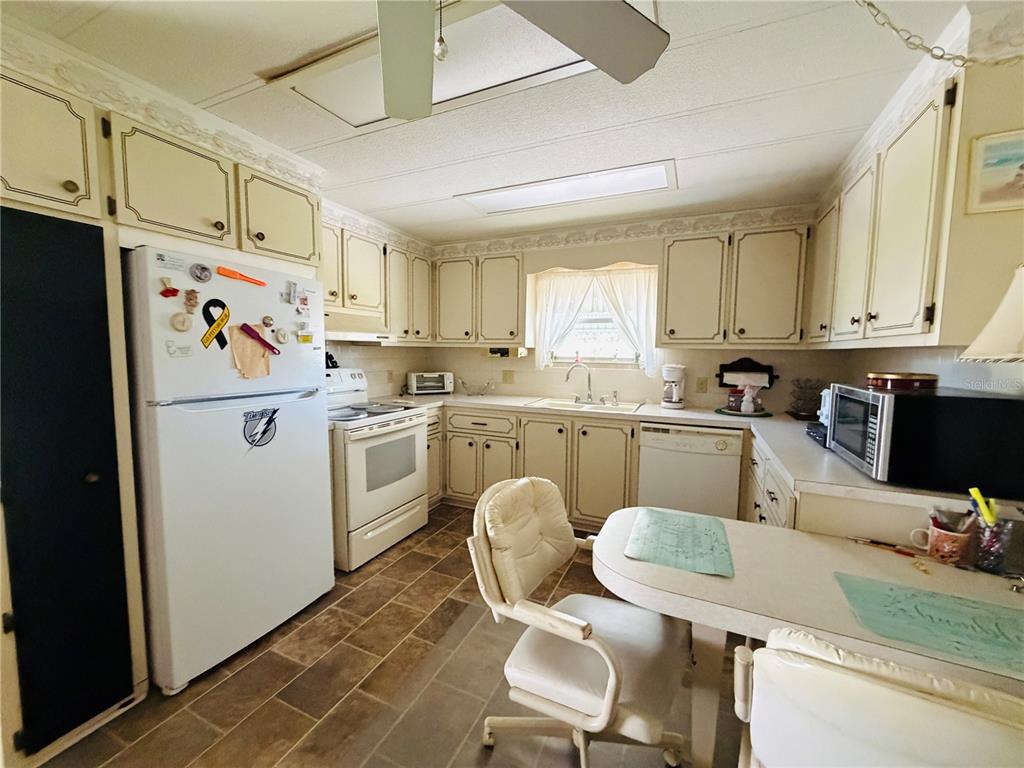 A kitchen features off-white cabinets, a white refrigerator, a small dining table, and tile flooring — 2331 BELLEAIR ROAD UNIT 206, CLEARWATER, FL