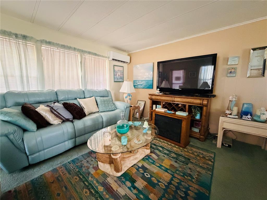 A living room features a blue sofa, a glass coffee table, and a television console — 2331 BELLEAIR ROAD UNIT 206, CLEARWATER, FL