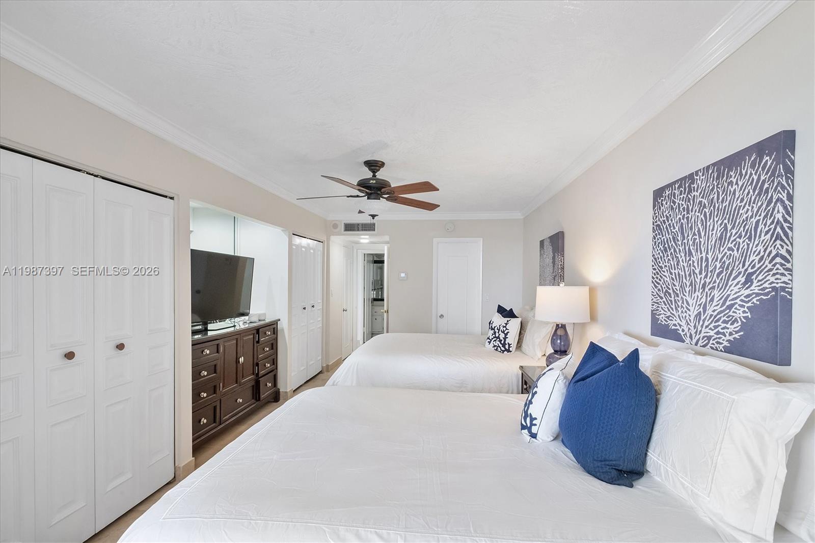 A bedroom features two beds, a dark wood dresser with a television, and ceiling fan — 5555 Collins Ave # 11A, Miami Beach FL 33140, MIAMI BEACH, FL