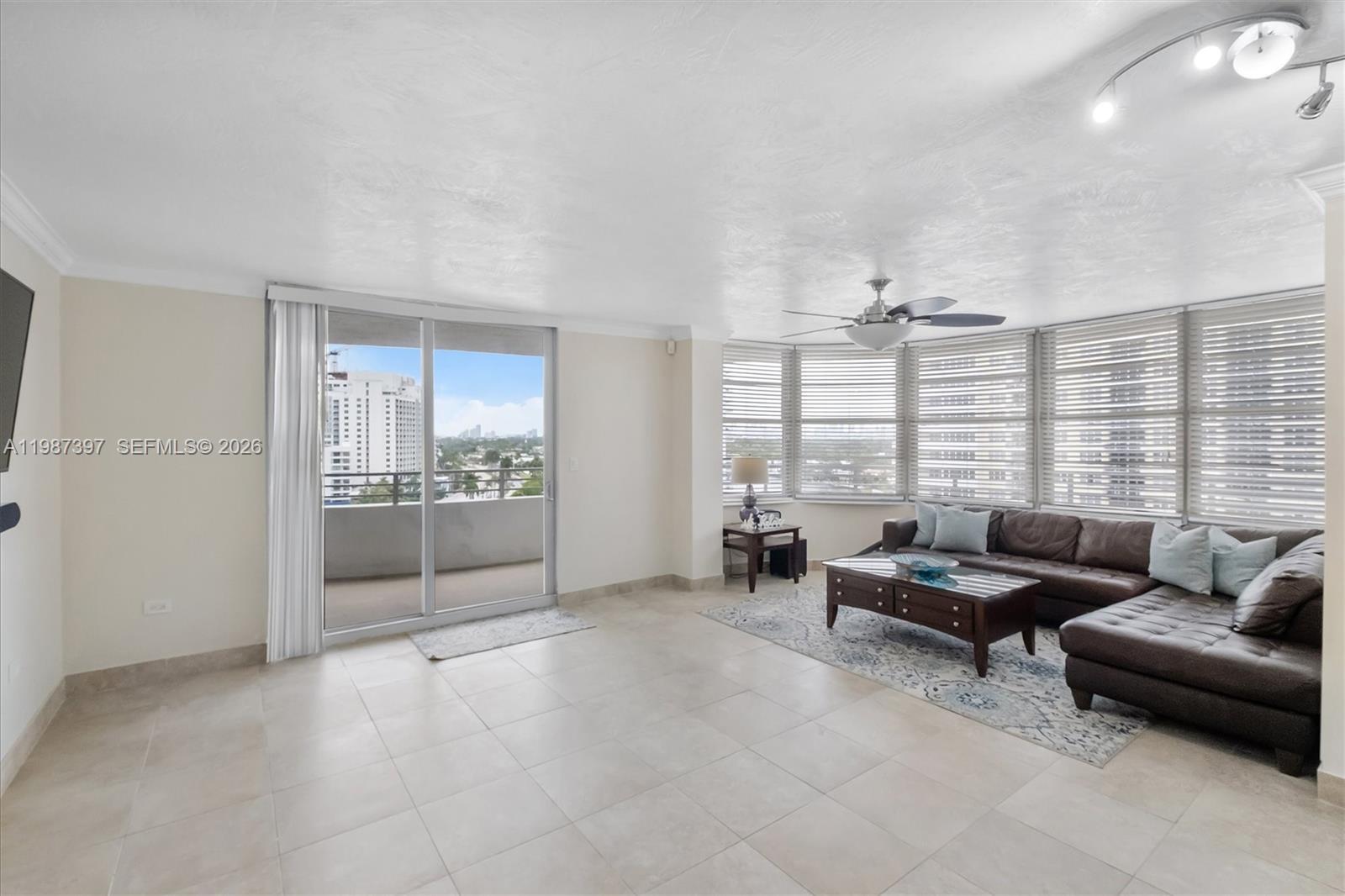 A living room features tile flooring, a large sectional sofa, and a balcony with city views — 5555 Collins Ave # 11A, Miami Beach FL 33140, MIAMI BEACH, FL