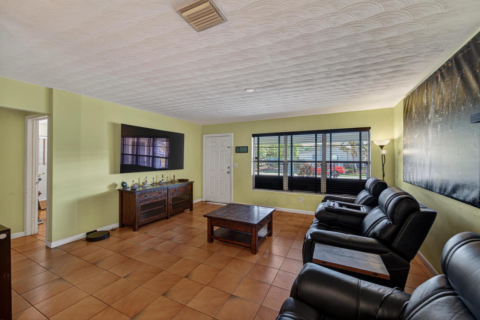 A living room features light green walls, tile flooring, a textured ceiling, and black leather recliners — 1211 NE 35th Street, Pompano Beach FL 33064, POMPANO BEACH, FL