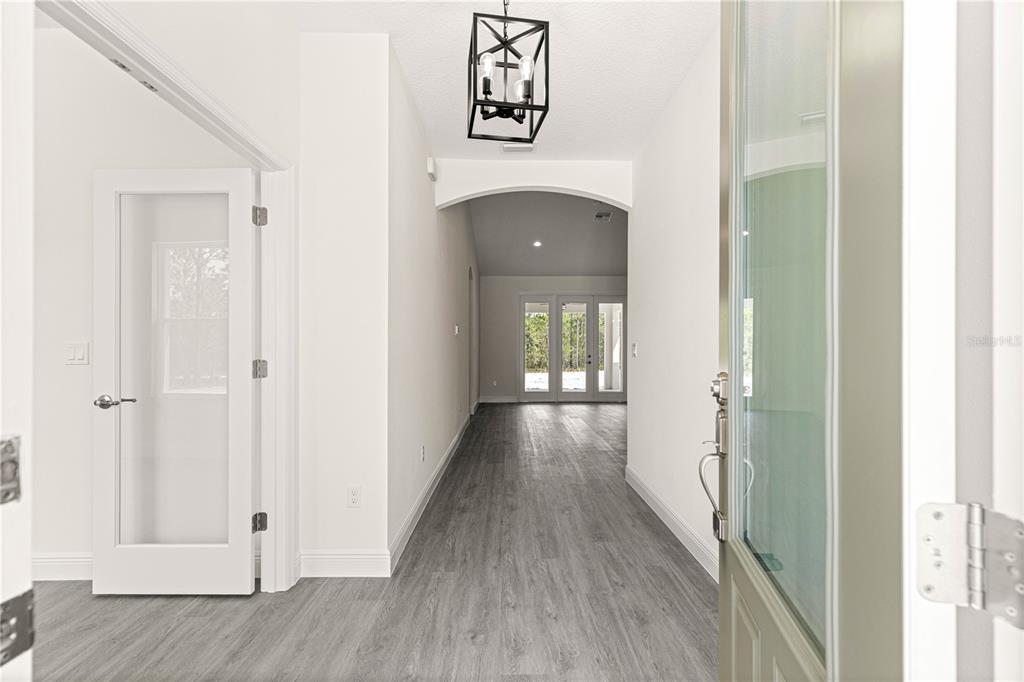 An empty room with light gray wood-look flooring, white walls, a tray ceiling, and windows — 12185 SW 98TH STREET, DUNNELLON, FL