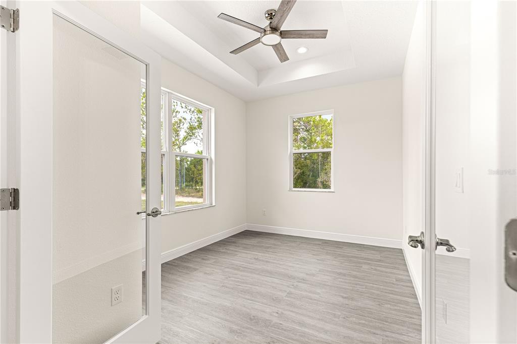 A room with light wood-look flooring, a tray ceiling, and a large window — 12185 SW 98TH STREET, DUNNELLON, FL