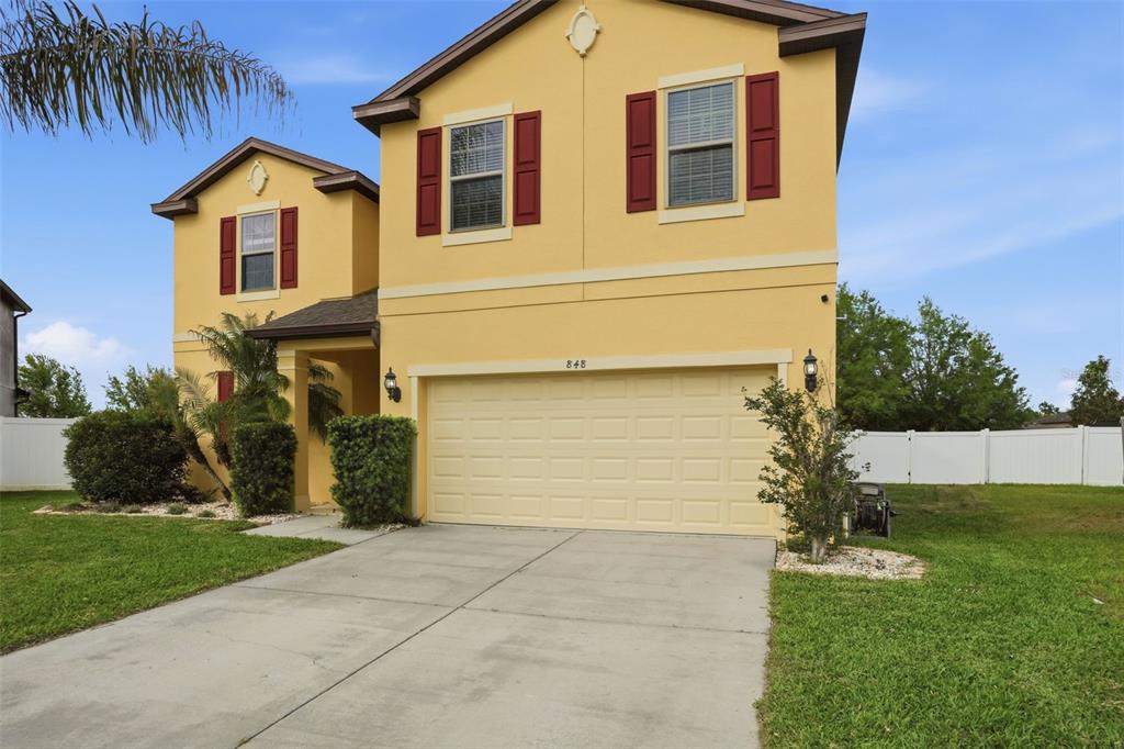 A two-story yellow house with a two-car garage and red shutters sits on grass — 848 PETAL MIST LANE, BROOKSVILLE, FL