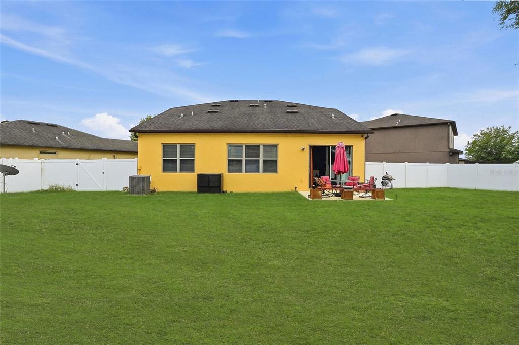 The rear exterior of a yellow house features a patio, lawn, and white vinyl fencing — 848 PETAL MIST LANE, BROOKSVILLE, FL