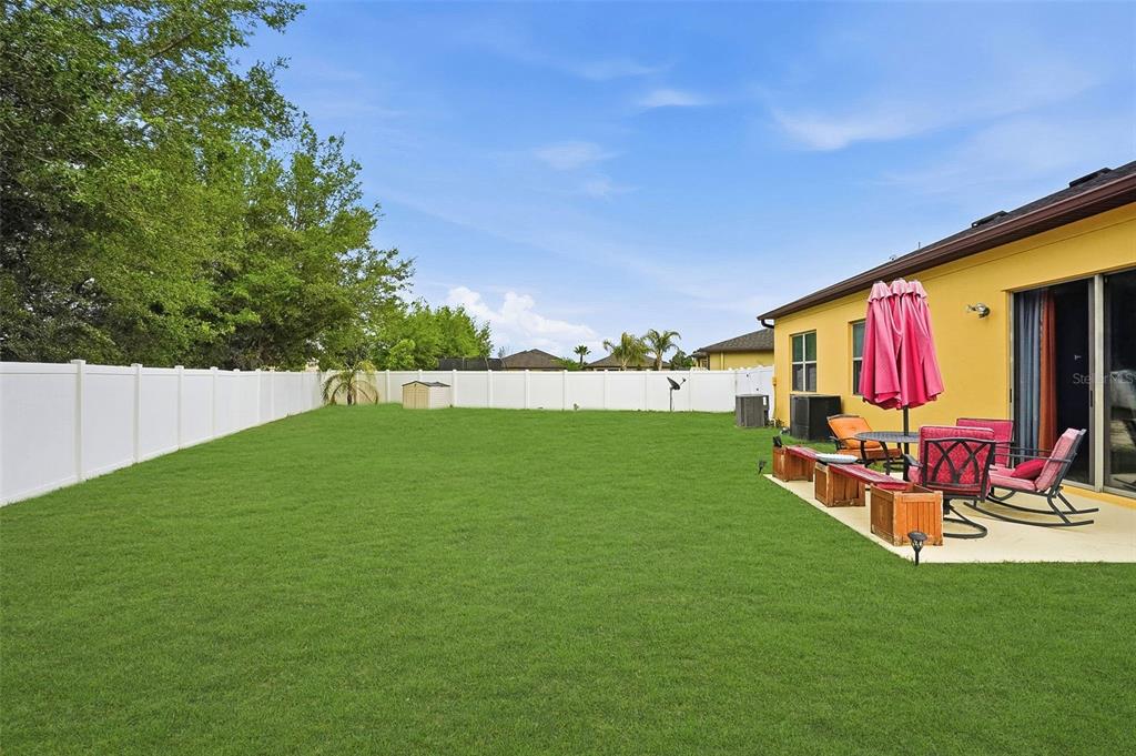 A backyard with a green lawn, white vinyl fence, and a concrete patio with furniture — 848 PETAL MIST LANE, BROOKSVILLE, FL