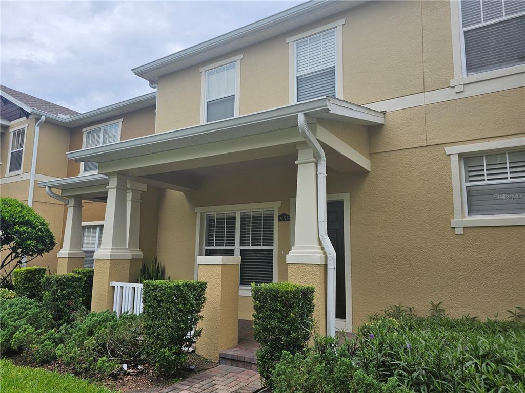 The exterior of a two-story tan townhouse features a covered front porch and landscaping — 9153 OAK FERN DRIVE, ORLANDO, FL
