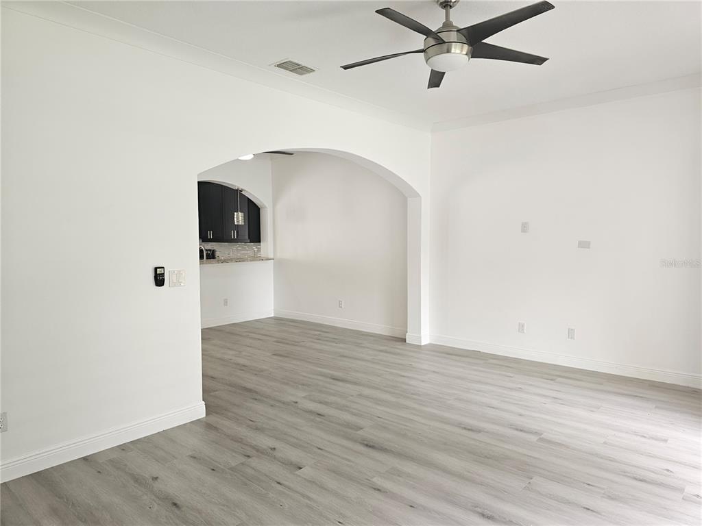 A living room with light wood-look flooring and an arched opening leading to a kitchen — 9153 OAK FERN DRIVE, ORLANDO, FL