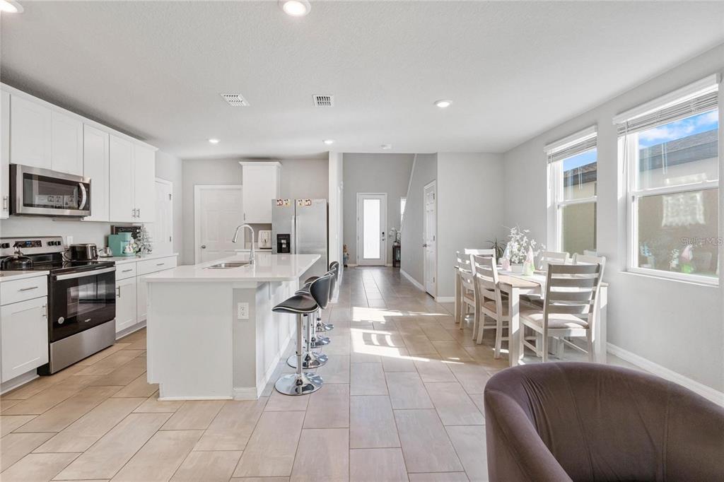 A modern kitchen features white cabinetry, a central island with bar seating, and a dining area — 17411 MILLION LAKES COURT, CLERMONT, FL